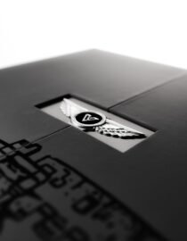 Close up of a dark surface with a silver winged logo partially visible set against a blurred light background