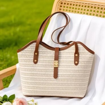 Beige woven tote bag with brown leather handles resting on a white chair Outdoors in a sunny garden