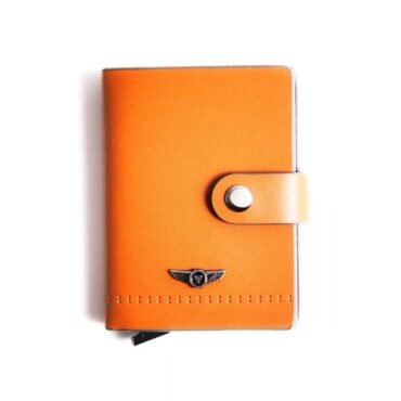 Close-up of an orange leather case or wallet with a silver strap and small winged emblem near the bottom edge