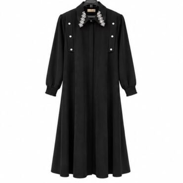 Black long-sleeve dress with a pleated A-line skirt, silver buttons on the bodice, and a jeweled collar on a hanger.