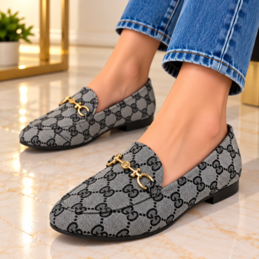 Gray designer loafers with a repeating GG pattern and gold horsebit detail, worn with cuffed jeans on a marble floor.