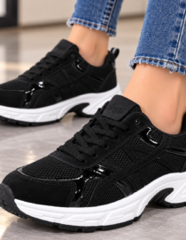 Black athletic sneakers with a white chunky sole on a tiled floor worn with frayed jeans