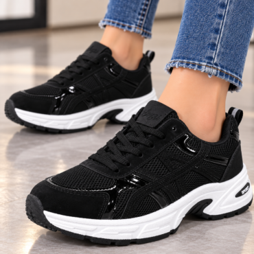 Black athletic sneakers with a white chunky sole on a tiled floor, worn with frayed jeans.