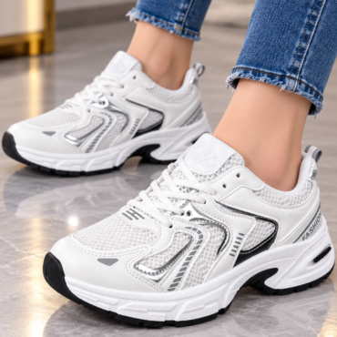 White chunky sneakers with mesh panels worn with cuffed blue jeans, shown in a close-up indoors.