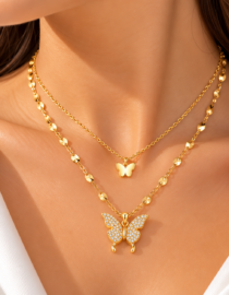 Close up of a womans neck wearing three layered gold necklaces with butterfly pendants the largest butterfly is encrusted with crystals on the chest area