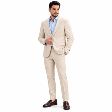 Man in a light beige suit with a blue dress shirt, standing with one hand adjusting the jacket.