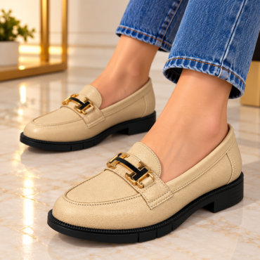 Beige leather loafers with black soles and gold horsebit detail, worn with rolled-up denim jeans on a marble floor.