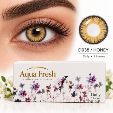 Close-up of a brown-eyed person wearing honey-colored contact lenses; Aqua Fresh Daily colored contact lenses box is in the foreground.