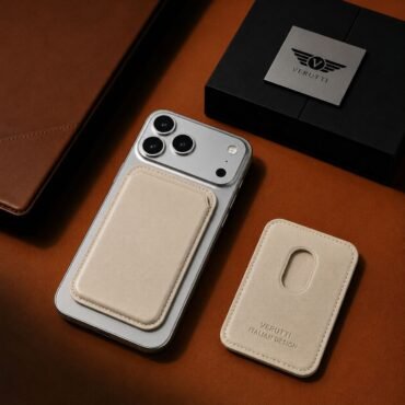 Silver iPhone with a beige leather card holder attached to the back, next to a matching beige case and a Verutti box on a brown surface.