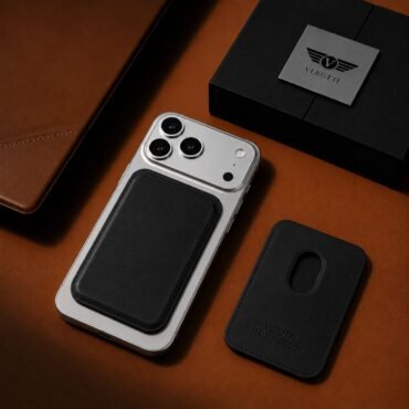 iPhone with a black leather card pocket attached to its back on a brown leather surface, with a Verutti box nearby.