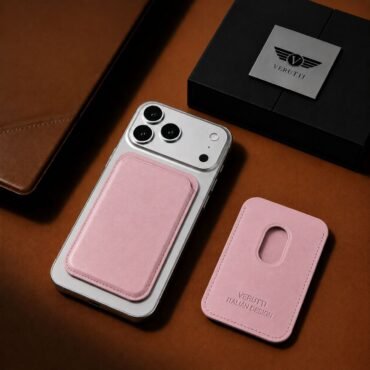 Silver iPhone with a pink leather back cardholder attached, paired with a separate pink phone case on a brown leather surface.
