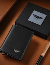 Black leather wallet with a small metal winged emblem laid on a brown surface beside a Verutti gift box and gold accented pen