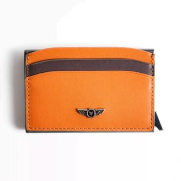 Close-up of an orange and dark brown leather wallet with stitched edges and a small metal winged crest emblem.