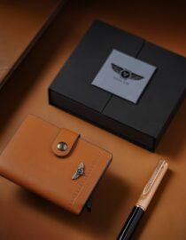 Close up of a tan leather item with stitched edges a small silver winged emblem and a black box on a warm brown surface