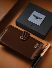 Brown leather wallet and a dark box placed on a tan leather surface with a patterned strap nearby